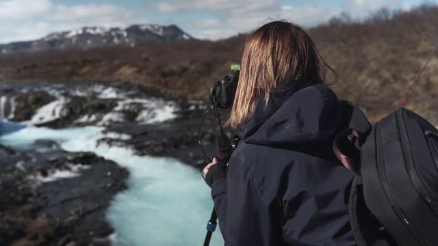 Female photographer taking amazing images of the waterfall Bruarfoss in Iceland. Recorded from behind.