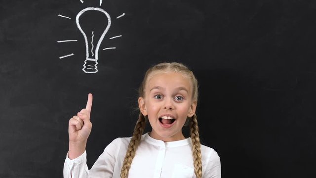 Inspired little girl pointing finger into bulb painted on blackboard, creativity