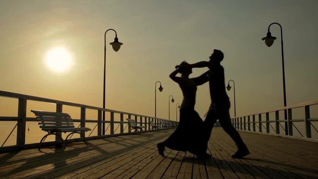 Dancing couple on the boardwalk in silhouette at sunset