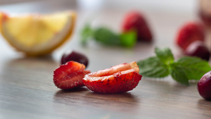 A piece of strawberry on a wooden background with a leaf of mint, cherry and   lemon in the background