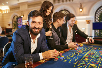 A man in a suit with a glass of whiskey sitting at table roulette playing poker at a casino.