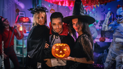 Halloween Costume Party: Father Count Dracula Holds Little Bat Girl Daughter and Hugs Witch Wife for a Happy Family Portrait. In the Background Monsters Having Fun