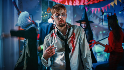 Halloween Costume Party: Young Businessman Zombie Doing Dead Dance, In the Background Beautiful Witch, Gorgeous She Devil and Scary Death and Count Dracula Dancing in the Decorated Room