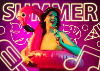 Female model in neon light on purple background. Modern design. Beautiful young woman in cap and sunglasses with icecream and swimring. Concept of facial expression, summer, vacation, music, open-air.