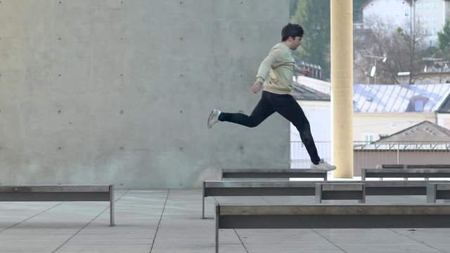 Young adult parkour athlete jumping from a bench to a bench in an urban environment in slowmotion