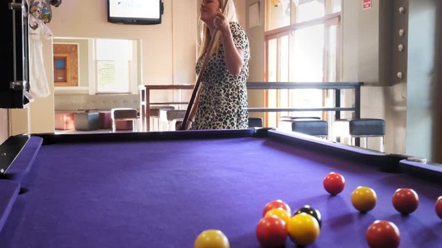 Young attractive blond woman playing pool table, also known as snooker or billiards.