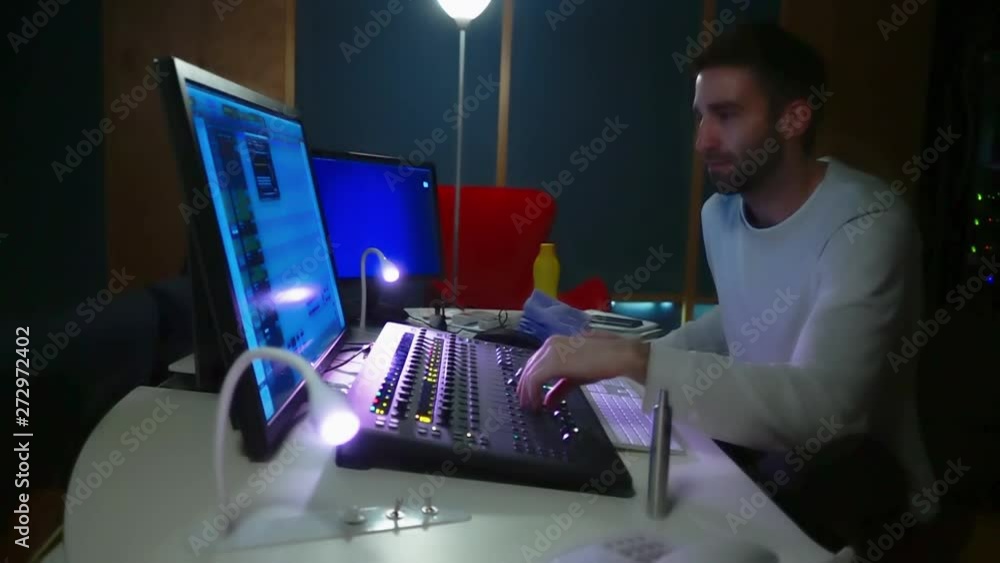 Poster shot of a sound engineered working on a studio using a mixer console and a computer surrounded by so