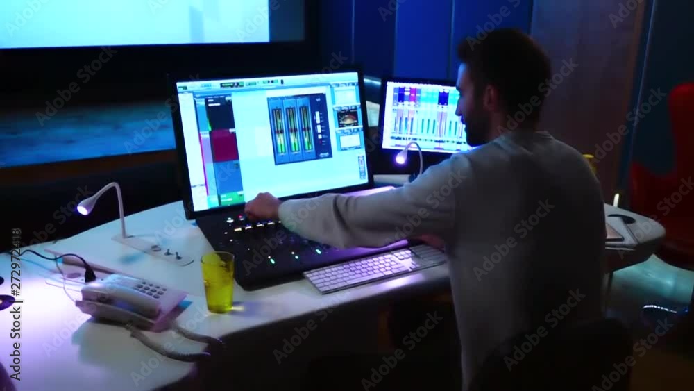 Poster shot of a sound engineered working on a studio using a mixer console and a computer surrounded by so