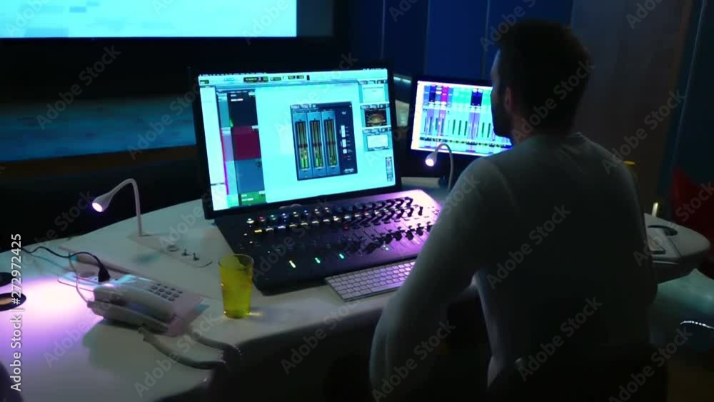 Poster shot of a sound engineered working on a studio using a mixer console and a computer surrounded by so