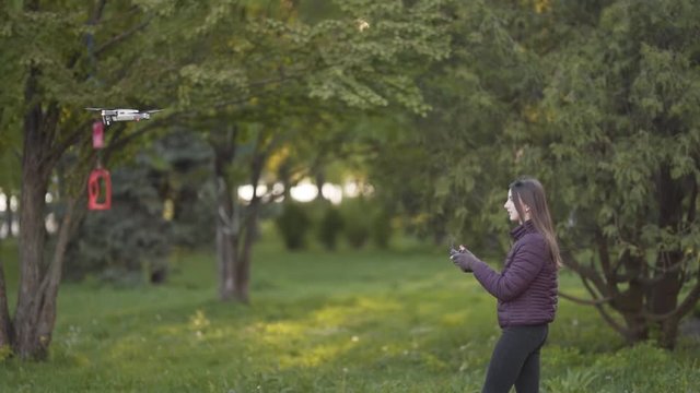 Cauciasan Female in Purle Jacket Following Drone and Tries to Catch Him in Public Park. Blurred Background