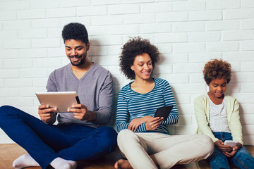 Family sitting in front of a brick wall and holding a digital tablet and phones