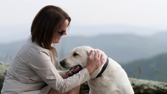 Woman pets white lab dog with mountains in background