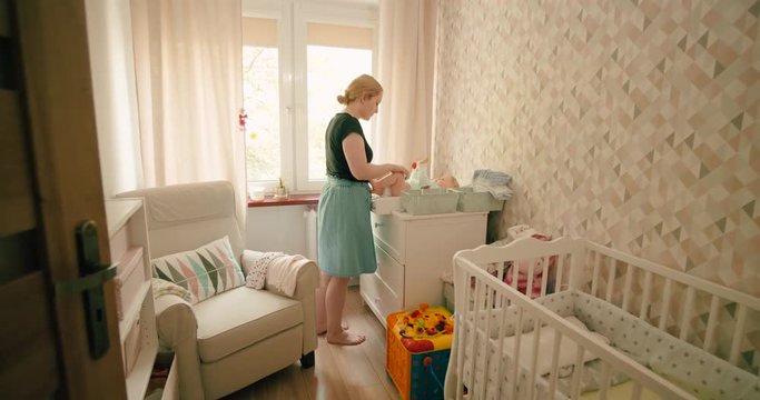 Mother changing the diaper of her baby girl at home on a baby changing table, dolly in