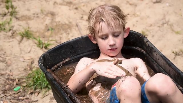 young boy covering chest in mud in wheelbarrow filled with water