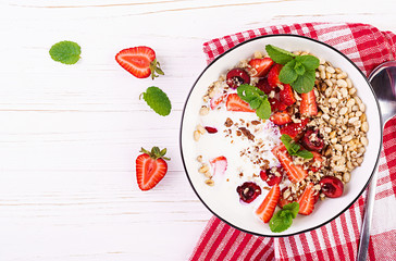 Healthy breakfast - granola, strawberries, cherry, nuts and yogurt in a bowl on a wooden table. Vegetarian concept food. Top view