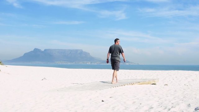 A tourist walks to the edge of a boardwalk in front of world famous Table Mountain, then sits down to enjoy the view.