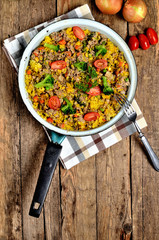 View from above of tuna risotto with vegetables, tomatoes, broccoli and parsley in the old pan, onions, cans and oil in the background - vertical photo