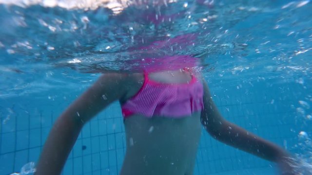 Close up footage of a toddler girl swimming underwater in a swimming pool