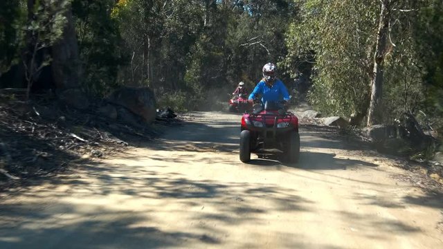 Driver facing slow motion shot of a blond woman riding a red quadro bike followed by a group of other quadro bike riders on a forest trail in Freycinet National Park