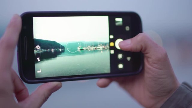 Close up of a woman's hands taking landscape photos of a bay with her smart phone