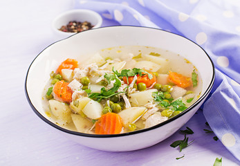 Chicken soup with green peas, carrots and potatoes in a white bowl on a light background.