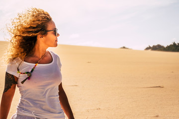 Beautiful blonde curly long hair young adult woman enjoy freedom and independence in outdoor leisure activity with desert sand in background - travel and discover scenic place concept