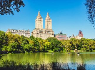 Obraz na płótnie Canvas Central Park Lake and Upper West Side. Beautiful greenish colors of the forest vegetation and boat rides through the beautiful lake. View of Manhattan skyscrapers.