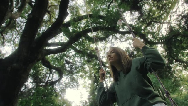 low angle shot from the side of girl on the shing under the dark forest tree