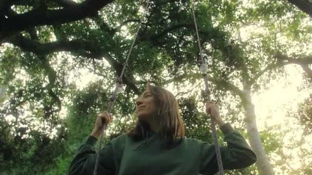 girl swinging on the swings and looking away with good mood and smile on her face enjoying evening in beautiful forest
