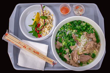 Vietnamese street food, pho bo soup with greens and rice flour noodles, plastic tray served with a large bowl of soup Hanoi street food, Vietnamese cuisine, top view