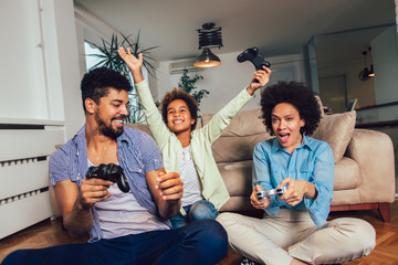 Smiling family sitting on the couch together playing video games, selective focus.