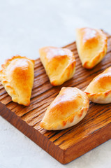 Homemade potato stuffed empanadas on a wooden board.