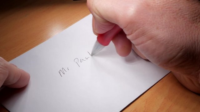 Man writes an address on a white envelope.