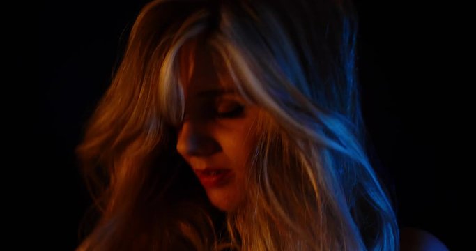 Young woman flips hair around and dances in night club; close up dramatic light.