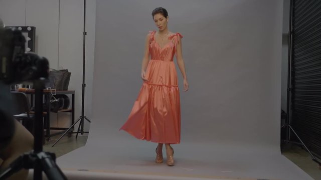 Woman fashion model swishing dress for photographer, studio photoshoot