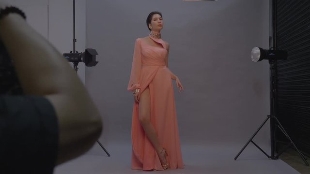 Fashion model woman in elegant dress posing for photographer in studio