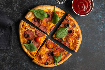 Cut into slices delicious fresh pizza with pepperoni on a dark background. Top view . Pizza on the black table.