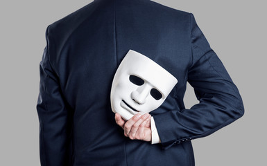 Business fraud concept. Businessman hide the mask in hand behind his back.
