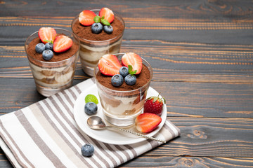 Classic tiramisu dessert with blueberries and strawberries in a glass on wooden background