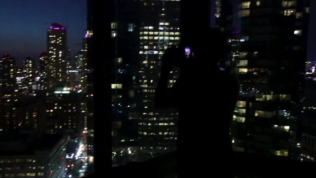 Silhouetted tourist taking pictures in a dark hotel room with a view