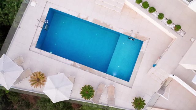 Rotating Upwards Aerial Shot of an Empty Pool of a Luxury Greek Villa with Miniature Palm Trees & Sun Loungers