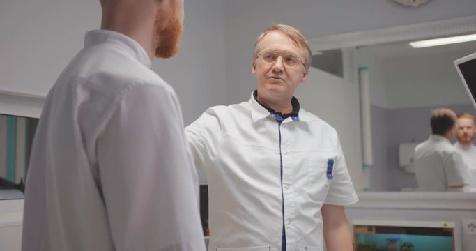 Smiling surgeon telling with therapeutic at meeting and patting his shoulders