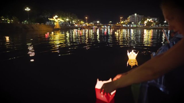Blonde tourist girl releasing a paper lantern from the boat, on the river in Hoi An, Vietnam at night