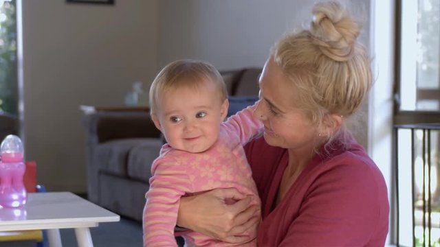Slow motion shot of a young blonde haired mom holding a smiling baby girl