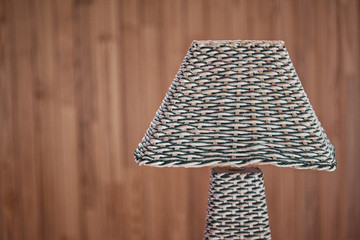 Gray decorative wicker lamp on a wooden wall background with place for text