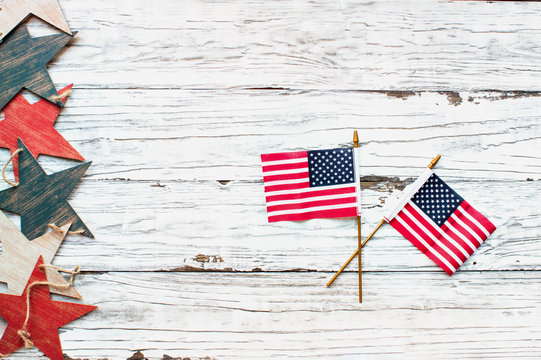Fourth of July Background. Two American flags and a border of a wooden star banner over a rustic white wood table / background to mark America's Independence Day. Image shot from top view.
