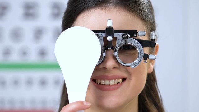 Smiling woman in phoropter closing one eye, vision examination, health check