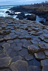 View of the Rocks of Giants Causeway with sea sprayed rocks and Ocean behind with tourists
