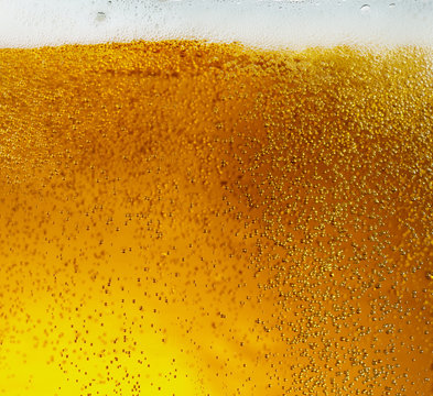 Close up view of floating bubbles in light golden colored beer background. Texture of cooling summer's filtered drink with foam and macro fizz on the glass wall. Fizzing or floating up to top of