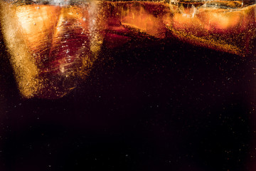 Close up view of the ice cubes in dark cola background. Texture of cooling sweet summer's drink with foam and macro bubbles on the glass wall. Fizzing or floating up to top of surface.